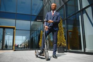 businessman with electric scooter standing in front of modern business building talking on phone. photo