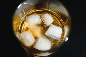 Glass of scotch whiskey and ice over black background photo