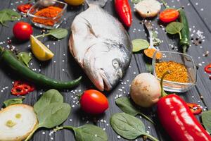 Fresh raw dorado fish on baking paper with lemon, pepper, tomatoes and various spices on wooden background with copy space. photo