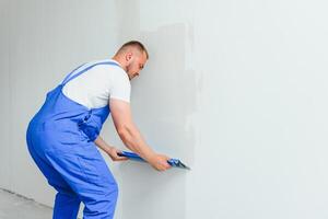 Portrait of a worker in overalls and holding a putty knife in his hands against the plastered wall background. Repair work and construction concept photo