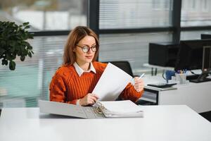 Young businesswoman sitting at workplace and reading paper in office photo