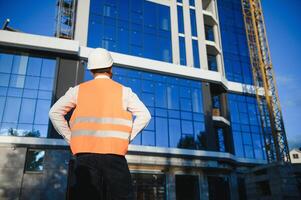 Engineer next to building cranes. Concept - large construction project. Architect directs the construction process. Drawings and tablet in the hands. photo