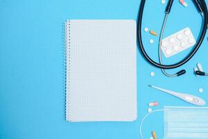 Scattered white pills on blue table.Medical, pharmacy and healthcare concept. Blue background white pills with a medical statoscope, top view photo