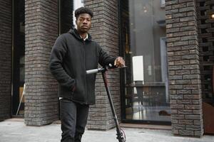 afro american guy rides an electric scooter against the background of a wall, a student uses eco transport photo