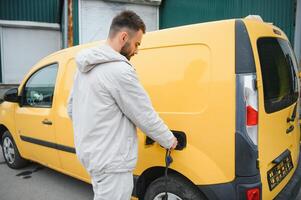 hombre participación poder cargando cable para eléctrico coche en al aire libre coche parque. y él s yendo a conectar el coche a el cargando estación en el estacionamiento lote cerca el compras centrar foto