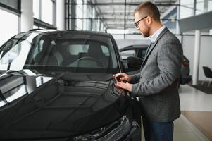 visitando coche concesión. hermoso barbado hombre es acariciando su nuevo coche y sonriente foto