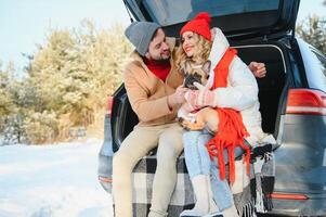 lovely smiling couple sitting in car trunk in winter forest photo