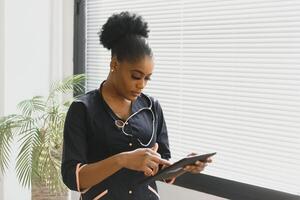 Portrait Of Smiling Female Doctor Wearing Scrubs In Hospital Corridor Holding Digital Tablet. photo