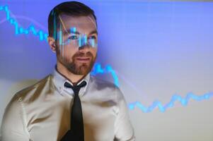 Stock Market Top Trader Looks at Projected Ticker Numbers and Graphs Running, Analysing Data to Make Best Sell. Behind Him Room Full of Screens and Statistics. photo