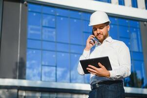 Engineer next to building cranes. Concept - large construction project. Architect directs the construction process. Drawings and tablet in the hands. photo