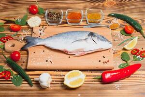 Fresh raw dorado fish on baking paper with lemon, pepper, tomatoes and various spices on wooden background with copy space. photo