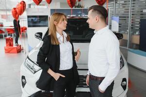 Young beautiful happy couple buying a car. Husband buying car for his wife in a salon. Car shopping concept photo
