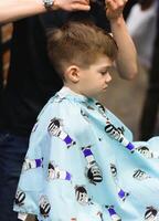 Cheerful Caucasian boy getting hairstyle in barbershop photo