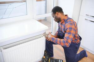 Man in workwear overalls using tools while installing or repairing heating radiator in room photo