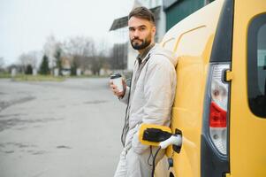 Casual man near electric car waiting for the finish of the battery charging process photo