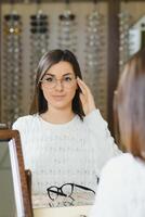 Row of glasses at an opticians. Eyeglasses shop. Stand with glasses in the store of optics. Woman chooses spectacles. Eyesight correction photo