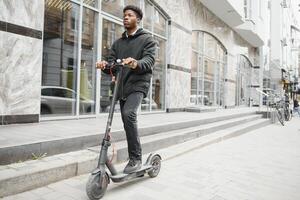 lleno cuerpo lado retrato contento africano americano hombre en móvil scooter en calle foto