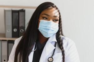 medicine, profession and healthcare concept - african american female doctor or scientist in protective facial mask in clinic. photo