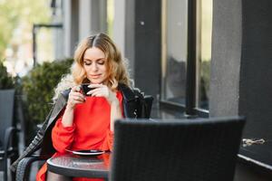 Fashion portrait of young woman siting at the table with cup of coffee, tea in street cafe. photo