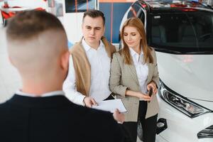 Happy young couple chooses and buying a new car for the family in the dealership photo