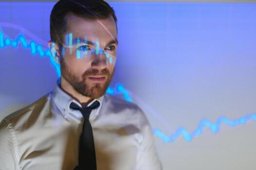 Stock Market Top Trader Looks at Projected Ticker Numbers and Graphs Running, Analysing Data to Make Best Sell. Behind Him Room Full of Screens and Statistics. photo