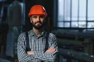 retrato de profesional pesado industria ingeniero trabajador vistiendo la seguridad uniforme, difícil sombrero sonriente. en el antecedentes desenfocado grande industrial fábrica. foto