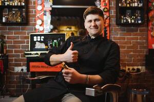 retrato de hermoso joven hombre en pie a Barbero tienda. elegante estilista en pie en su salón con su brazos cruzado. foto