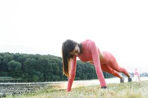 Push ups or press ups exercise by young woman. Girl working out on grass crossfit strength training in the glow of the morning sun against a white sky with copyspace. Mixed race Asian Caucasian model. photo