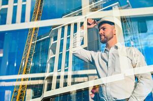 Engineer next to building cranes. Concept - large construction project. Architect directs the construction process. Drawings and tablet in the hands. photo