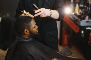 de cerca de proceso de guarnición de pelo en Barbero tienda. calificado Barbero acuerdo clíper en manos y de corrección forma de pelo a masculino cliente sentado en silla. concepto de Corte de pelo y afeitado. foto