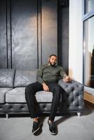 Handsome young african american man in elegant suit with glass of whiskey relaxing on sofa photo