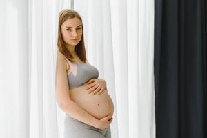 Young beautiful pregnant woman standing at home near the window. photo