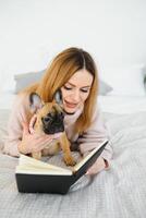 joven mujer con perro y libro relajante adentro a hogar, lectura. foto