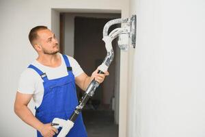 Plasterer smoothes the wall surface with a wall grinder. Master builder grind a white plaster wall. a man in overalls grinds the surface in a respirator. experienced repairman photo