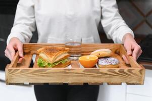 Young woman holding tray with breakfast food at home photo