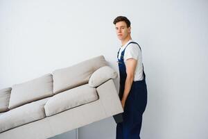 Loader moves sofa, couch. worker in overalls lifts up sofa, white background. Delivery service concept. Courier delivers furniture in case of move out, relocation. photo