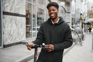 joven africano americano chico con eléctrico scooter en el ciudad. el concepto de ecológico transporte. foto