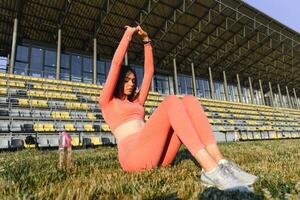 deporte y bienestar. aptitud niña haciendo extensión ejercicio. Moda deportivo mujer con fuerte muscular cuerpo capacitación. ajuste hembra extensión a al aire libre estadio foto