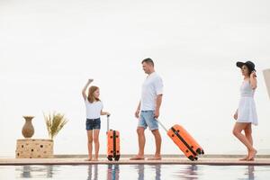 young family with suitcases walking to hotel building with beautiful swimming pool. traveling and relaxing time concept. photo