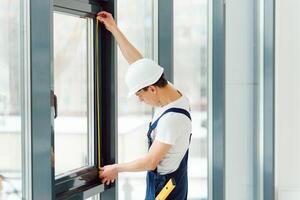 Workman in overalls installing or adjusting plastic windows in the living room at home photo