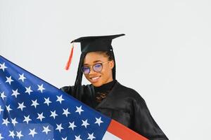 Charming female student smiling in eyeglasses wearing black mantle and standing with American flag photo