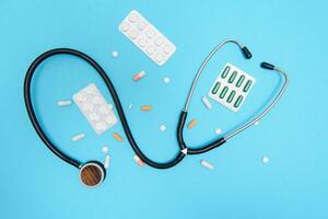 Scattered white pills on blue table.Medical, pharmacy and healthcare concept. Blue background white pills with a medical statoscope, top view photo