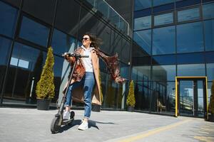 Young beautiful woman riding an electric scooter to work, modern girl, new generation, electric transport, ecology, ecological transport, sunset, electric skateboard. photo