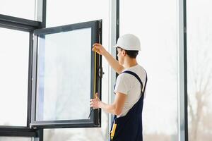 Workman in overalls installing or adjusting plastic windows in the living room at home photo