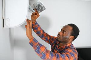 African American electrician repairing air conditioner indoors photo