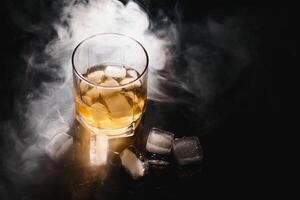 whiskey with ice on black background with smoke photo