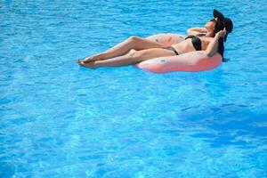 Beautiful young woman with inflatable donut in blue swimming pool photo
