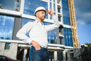 Engineer next to building cranes. Concept - large construction project. Architect directs the construction process. Drawings and tablet in the hands. photo