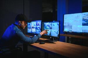 Rear view of security system operator looking at CCTV footage at desk in office photo