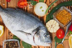 Fresh raw dorado fish on baking paper with lemon, pepper, tomatoes and various spices on wooden background with copy space. photo